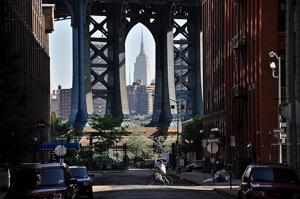 A delivery man bikes early in the morning on Washington Street in DUMBO, Brooklyn, with the Manhattan Bridge and the Empire State Building in the background.